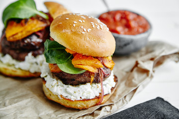 Burgers with grilled beef patties, cream cheese and spinach on classical bun. White wooden...