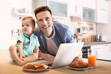 Young father with his cute little son using laptop in kitchen