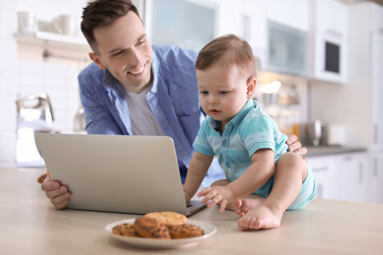 Young father with his cute little son using laptop in kitchen