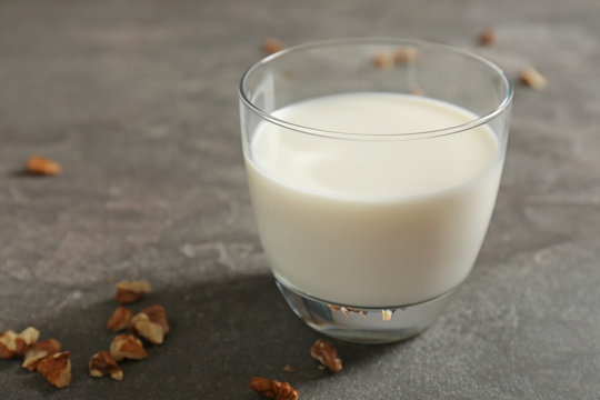 Glass with milk and nuts on grey background