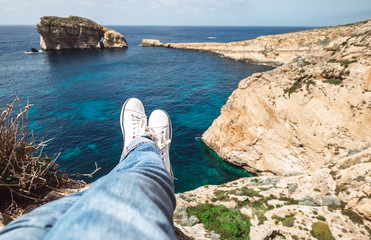 Traveler's feet in white sneakers on the edge of rocky seaside