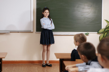 Smiling elderly teacher near the chalkboard asking student at the math lesson