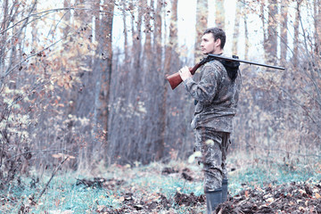 Naklejka premium A man in camouflage and with a hunting rifle in a forest on a sp