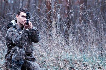 A man in camouflage and with a hunting rifle in a forest on a sp