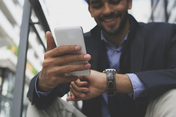 Businessman on city street checking time and using smart phone. Focus is on hands.