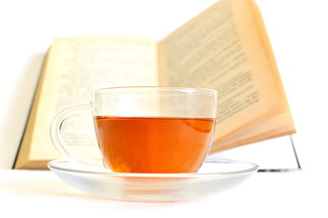 hot black tea in transparent glass cup on saucer and open book on white background