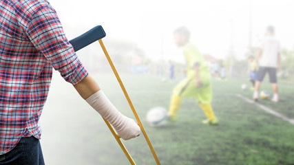 Injured sport player with wrist support or arm cast on hand and arm isolated on blurred kid soccer player in football field, clipping path included