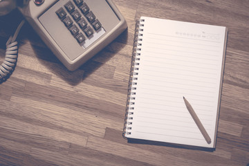 Small pencil on blank notebook with vintage dial phone on wooden table