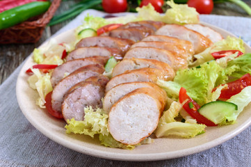 Juicy home made sausage with a light spring salad of fresh vegetables on a wooden table. A traditional Easter dish. Close up