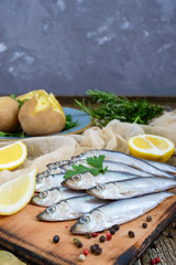 Boiled unpeeled potatoes in skins, a small salted fish of Baltic herring, sprats on a wooden table