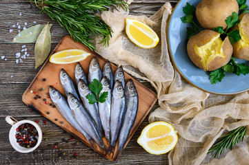 Boiled unpeeled potatoes in skins, a small salted fish of Baltic herring, sprats on a wooden table. Top view. Flat lay - obrazy, fototapety, plakaty