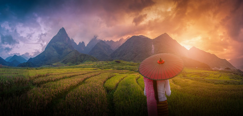 Woman holding traditional red umbrella on rice fields terraced at sunset in Sapa, Vietnam.