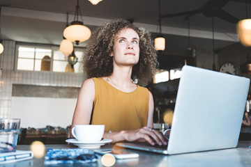 Pretty woman typing on laptop. Sitting in city cafe with cup of coffee and mobile device, inventing new ideas