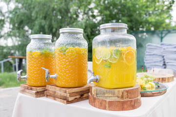 Glass bank of lemonade with sliced citrus fruits on a buffet table. Summer party outdoor. Detox.