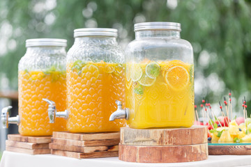Glass bank of lemonade with sliced citrus fruits on a buffet table. Summer party outdoor. Detox.