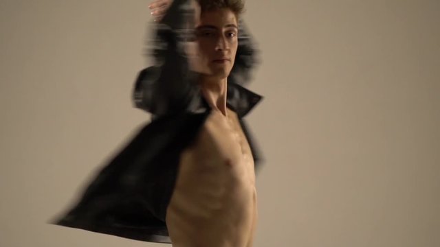 A sexy man in a black leather jacket is swirling around in front of the camera, slow motion