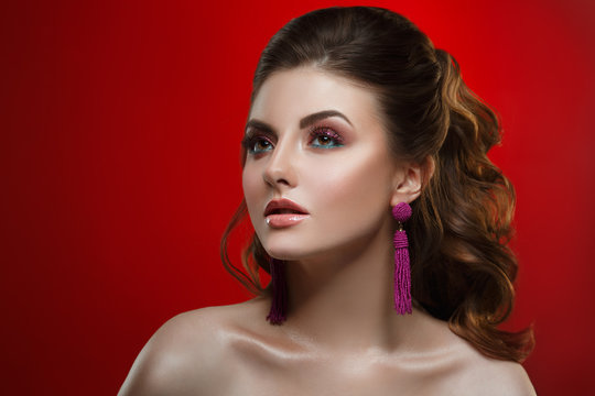 Fashion beauty portrait of a beautiful girl with a bright make-up and an elegant hairstyle on a red background.