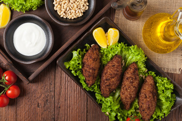 Traditional arabic kibbeh with lamb and pine nuts. Top view. Natural wooden background.