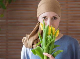 Young positive adult female cancer patient holding bouquet of yellow tulips, smiling and looking at...