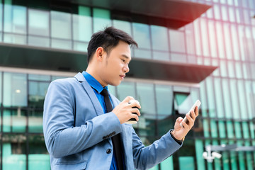 Asian young businessman drinking morning coffee and reading phone on urban