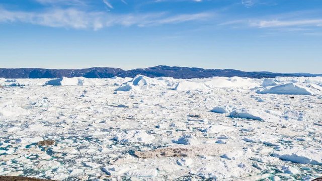 Travel in arctic landscape nature with icebergs - Greenland tourist man explorer - tourist person looking at amazing view of Greenland icefjord - aerial video. Man by ice and iceberg in Ilulissat.