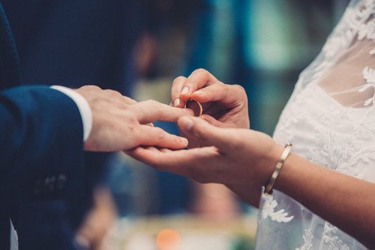 Close-up of bride placing ring on finger of bridegroom at wedding