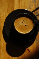 view of a cup of black coffee in a black cup with a lot of krema, on a timber table
