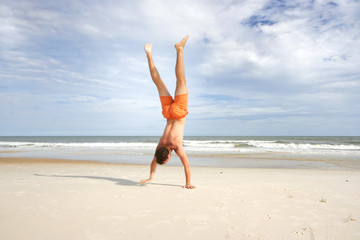 Fototapeta na wymiar Young man in orange swim suit making hand stand on a sandy beach