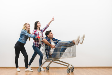 The three happy people with a shopping cart gesture on a white wall background - Powered by Adobe