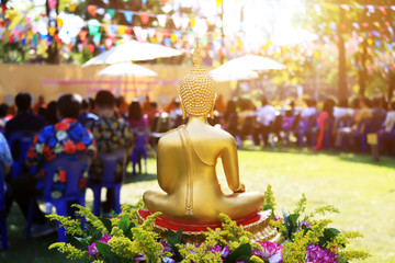 Back of golden buddha statue with people in Songkran festival celebration. 