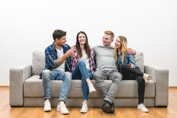 The four happy friends sit on the sofa on a white wall background
