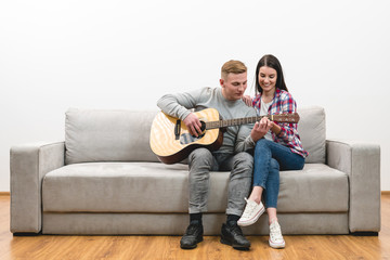 The couple sit on the sofa and play the guitar on the white wall background