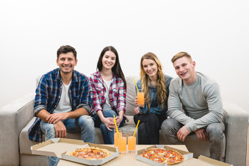The happy friends with a pizza and drinks sit on the white background