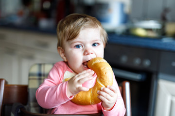 Cute little baby girl eating bread. Child eating for the first time piece of pretzel.