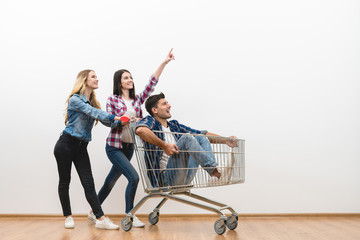 The three happy people with a shopping cart gesture on a white wall background
