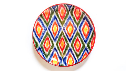 traditional ceramic Uzbek utensils -  plate with ornament Ikat on white background Top view