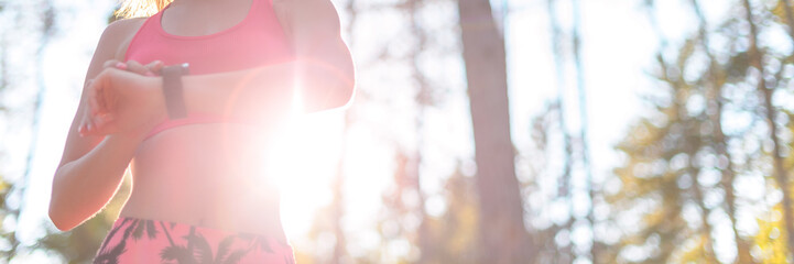 Young attractive sportswoman listening to music wearing headphones and checking her smart watch. Sport, fitness, workout concept. Blurred Web banner.