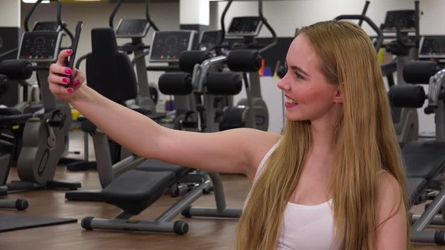 A young beautiful woman takes selfies in a gym
