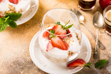 Healthy breakfast with oatmeal granola, strawberries and yogurt on light brown background. Copy space.