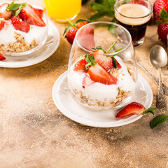 Healthy breakfast with oatmeal granola, strawberries and yogurt on light brown background. Copy space.