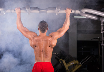 Fototapeta na wymiar Athlete muscular fitness male model pulling up on horizontal bar in a gym.