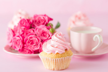 Cupcake with pink cream decoration and roses on pink pastel background.