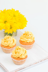 Cupcake with tender yellow cream decoration and bouquet of chrysanthemum in glass on yellow pastel background.