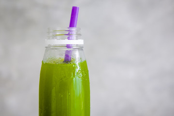 Plastic bottle of cold-pressed green juice with purple straw against gray wall. Body cleance, fast, detox concept. Minimalism food photography. Copyspace