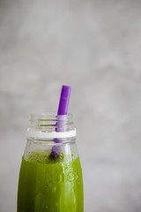 Plastic bottle of cold-pressed green juice with purple straw against gray wall. Body cleance, fast, detox concept. Minimalism food photography. Copyspace