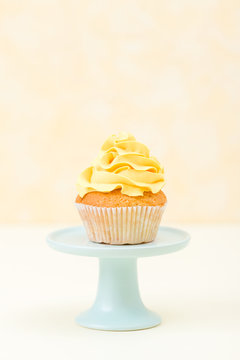 Cupcake with yellow cream decoration on blue stand on yellow background - pastel vertical banner. Minimalism still life concept.