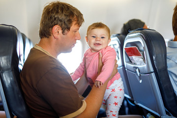 Young tired father and his crying baby daughter during flight on airplane going on vacations