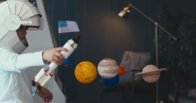 WIDE Cute little boy and girl siblings or friends wearing cardboard astronaut helmets flying toy rocket through planets, exploring deep space. 4K UHD 60 FPS SLOW MO
