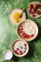 Sweet rice porridge pudding in ceramic plate with berries strawberry and raspberry, walnuts, honey and mug of milk over green texture background. Top view, space.