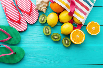 Summer fun time and fruits on blue wooden background. Orange, lemon fruit in bag and flip flops. Top view and copy space